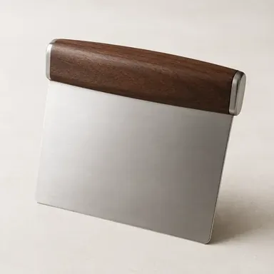 Stainless steel bench scraper with a black handle on a floured work surface