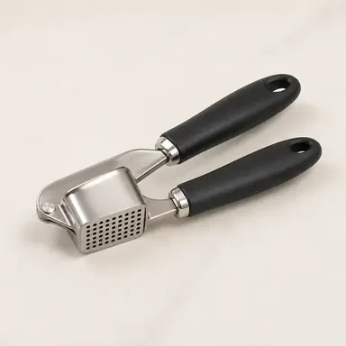 Stainless steel garlic press with black handles on a marble counter