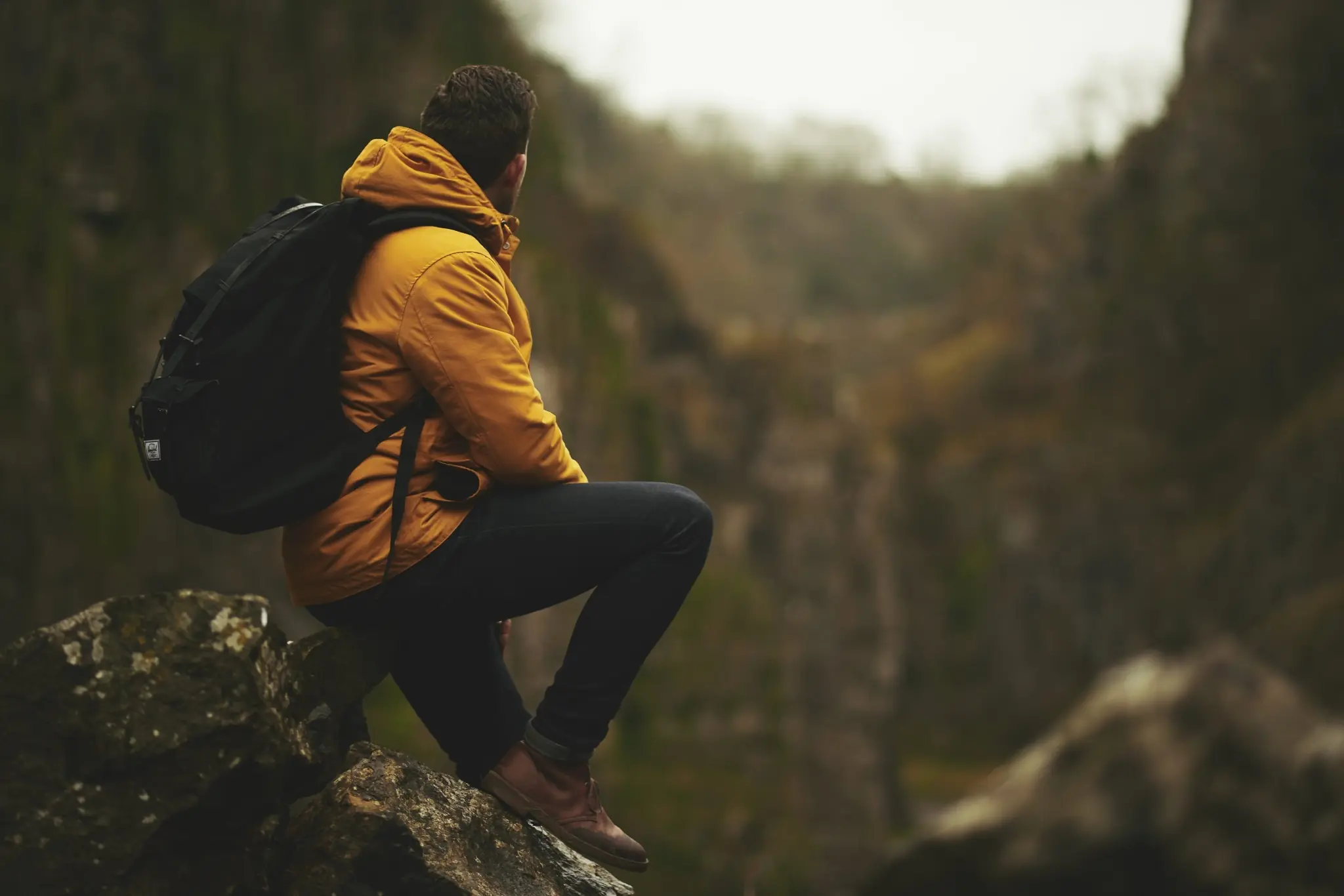 Hiker in a yellow jacket with a backpack sitting on a rock, looking out over a misty mountain valley