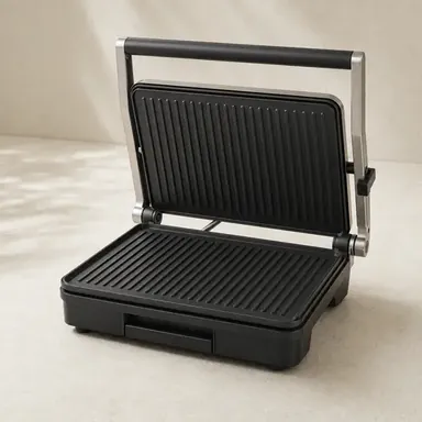 Open panini press with ridged stainless-steel and black grill plates on a light surface